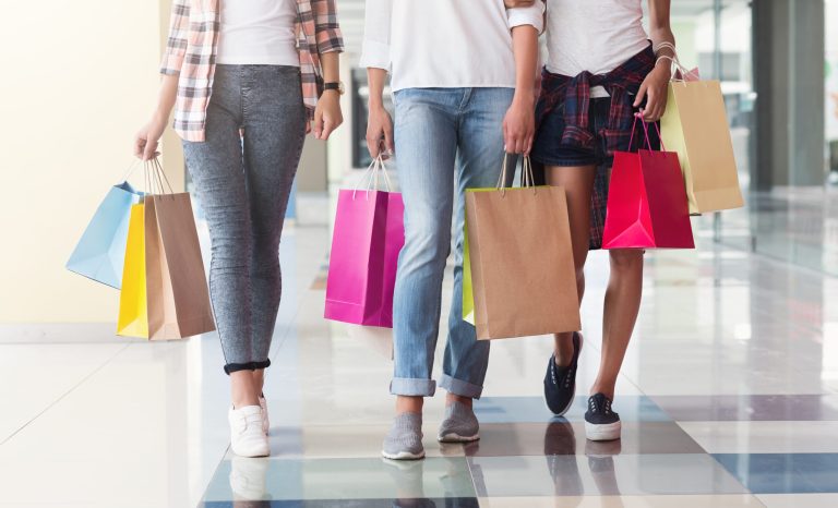 Three consumers with paperbags walking down shopping center